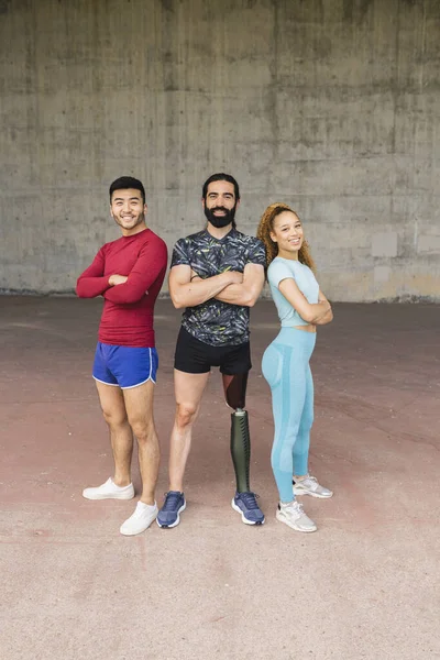 Full body front view of three multiracial athletes with arms folded. Man with orthopedic leg. Asian, hispanic and caucasian people