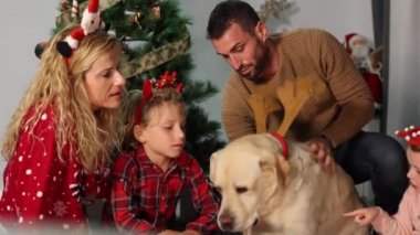 Labrador köpeğiyle mutlu bir aile yerde oturmuş Noel 'i kutluyorlar ve kameraya bakıyorlar..