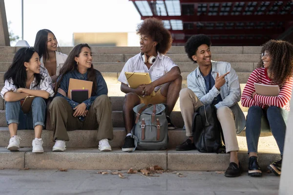Multiracial group of college students sitting on the stairs talking after class