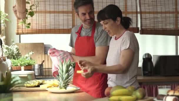 台所で大人の夫婦がパイナップルを分け合う 大人の夫婦が一緒に料理をするというコンセプトは — ストック動画