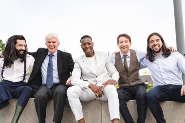 Farklı yaşlarda, takım elbiseli, kameraya bakarak poz veren mutlu, çok ırklı bir grup adam. Protez bacaklı genç bir adam.