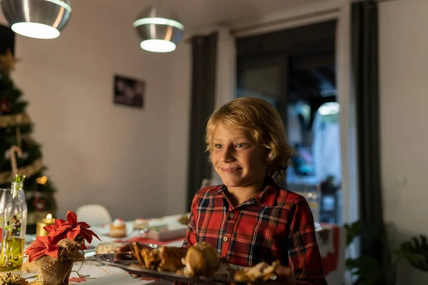 Caucasian blonde boy brings his family Christmas dinner to the table. Little boy helps his parents