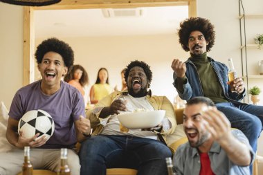 Çok ırklı bir arkadaş grubu televizyonda maç izleyerek zaferi kutluyor. Aşırı kilolu ve iri yarı Amerikalı Afrikalı erkeklere odaklan.