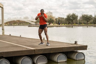 Kıdemli Afro-Amerikan adam göllü bir parkta boks antrenmanı yapıyor.