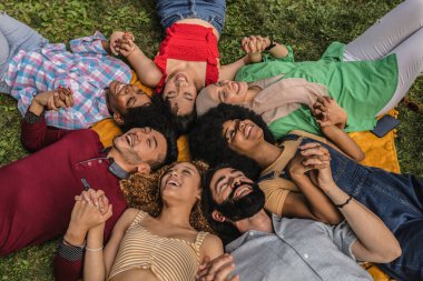 Çimlerin üzerinde el ele tutuşmuş çok ırklı gençler var.