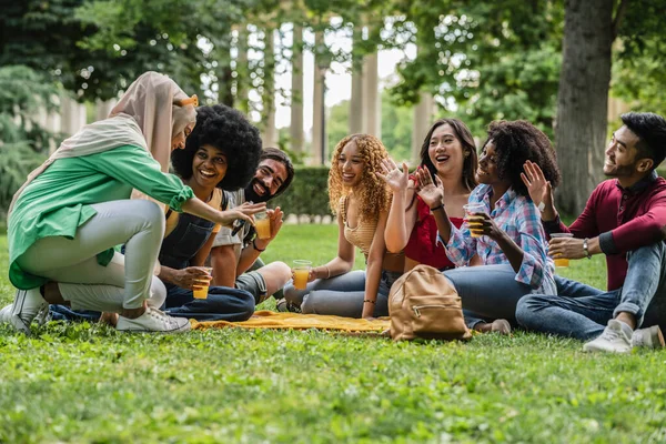 인종으로 이루어진 친구들 공원의 풀밭에 오렌지 주스를 마시며 흔들고 — 스톡 사진