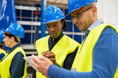 Güvenlik kaskı ve yansıtıcı yelekli iki çok ırklı işçi tablete işçi eylemleri yazıyor. Bir robot fabrikasında. Afrika kökenli Amerikalı adama odaklan.