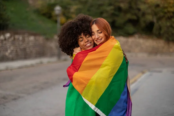 Två Multietniska Lesbiska Kvinnor Som Omfamnar Med Regnbågsflaggan Lgbtiq Gatan — Stockfoto