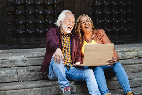 Multiracial Senior Couple Laughing Video Laptop Sitting Stairs Outdoors Happy — Stock Photo, Image