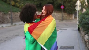 Çok ırklı lezbiyen çift birbirlerine aşkla bakıyor. Igbt özgürlük gökkuşağı bayrağıyla sarılıyorlar. Çeşitli insanlar birbirini seviyor.