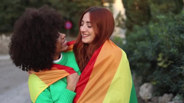 多人種間のレズビアンカップル見ますお互いとともに愛を受け入れますとともにザLbt虹旗でストリートで日没 — ストック動画