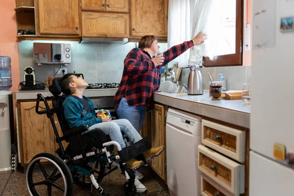 İspanyol anne engelli oğluyla birlikte mutfaktaki pencereden bakıyor. Aile, koşulsuz sevgi ve kapsama kavramı..