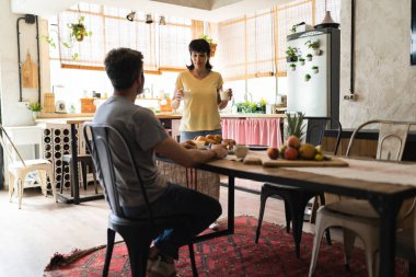 Olgun karı koca, kahvaltılarını ahşap mutfakta yapar. Kadın masaya bir bardak süt getirir..