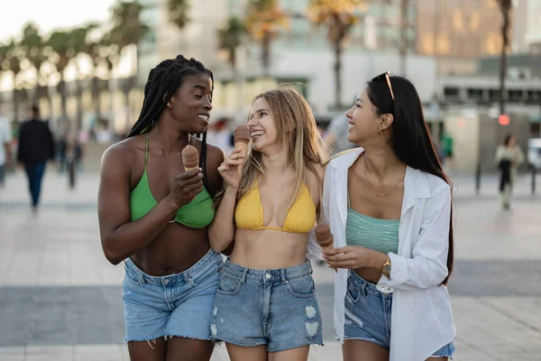 female friends in summer clothes eating ice cream on the street
