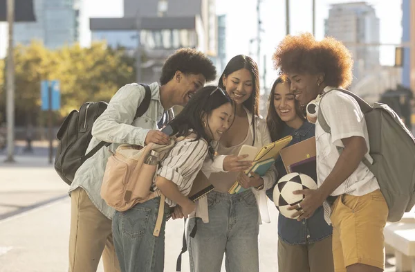 group of multiracial students looking at a smartphone in the street