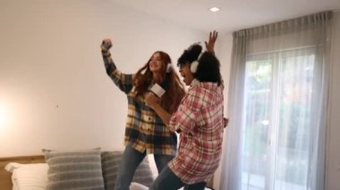 two multiracial women singing and jumping up on the bed