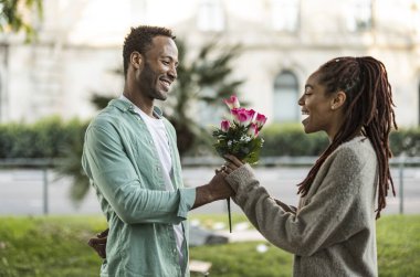 romantic man gives bouquet of flowers to his girlfriend in the street - she is surprised and happy -