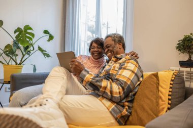 african senior couple at home video call tablet with family