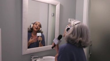 elderly woman sings in front of the bathroom mirror to practice while that music