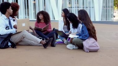 A group of multiracial students with sit on the steps near the campus and communicate.