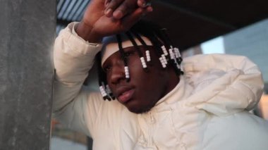 young african man with dreadlocks is leaning against a wall while looking at the horizon