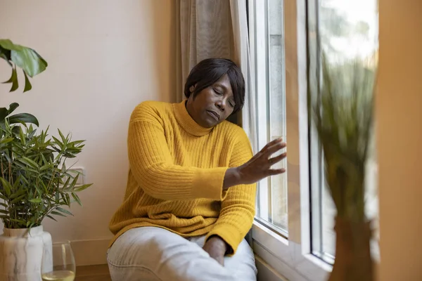 mature woman depression home - sad african american elderly woman looking out the window -