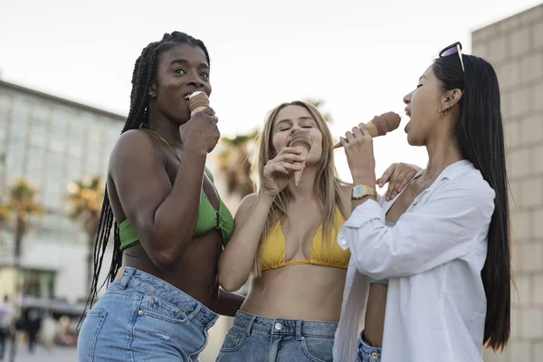 Female friends at the beach eating ice cream - multiracial women at the beach on summer vacation-
