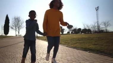 single mother with her little african american son running in the park on a sunny day