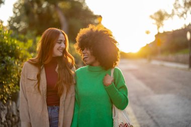 two multiracial women holding hands in the city, happy girls going to a concert at sunset