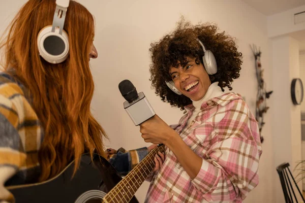 two multiracial women at home sing and dance with headphones and microphone