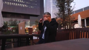 Yetişkin Kafkasyalı iş adamı internetteki uzak konferans görüntüleriyle sanal toplantı yapıyor. Bilgisayara bakıyor ve gece kafeteryasında ya da parkta oturup uzaktan Webinar izliyor..