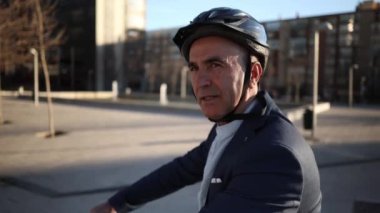 Şık takım elbiseli neşeli orta yaşlı işadamı dışarıda elektrikli scooter sürerken gülümsüyor.