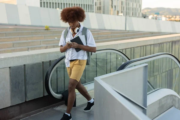 スマートフォンを持つ若いアフリカ人男性がエスカレーターで上ります 学生キャンパス — ストック写真