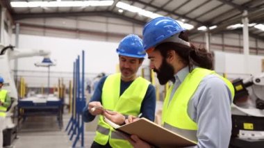 Robot fabrikasındaki erkek iş arkadaşları otomasyonun faydalarını ve zorluklarını tartışarak, devam eden eğitim ve işbirliği ihtiyacını vurguladılar..