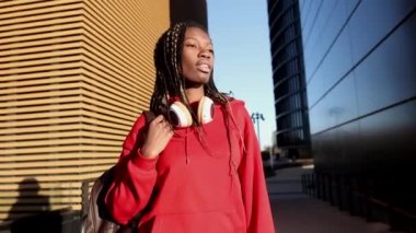 Güzel Afrikalı kadın rastalı, kırmızı günlük kıyafetler giyiyor, şehirde, sırt çantası ve kulaklık takıyor..