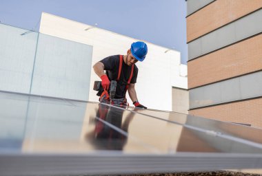 Bir binanın çatısına güneş panelleri kuran bir teknisyen, ekonomik enerji ve sürdürülebilirlik kavramı, küçük işletme