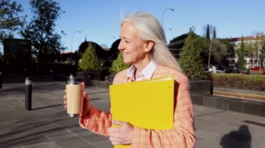 Zarif gri saçlı, kahve ve klasörlü olgun bir iş kadını. Gün doğumuna doğru yürüyor.