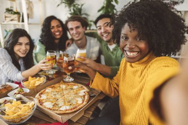 Mutlu arkadaş grubu, lokanta barında bira içerek selfie çekiyor, gençler akşam yemeği yiyor, pizza yiyor, yaşam tarzı kavramı, kadeh kaldırma, fotoğraf çekme, Afrikalı Amerikalı kadınlara odaklanıyor. -