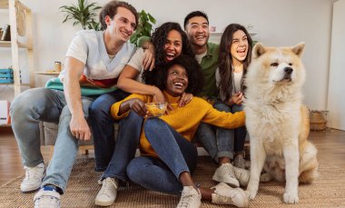 Kanepede köpekli bir grup genç kız - çok ırklı insanlar eğleniyor - ev arkadaşları, öğrenciler