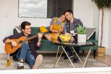 Arkadaşlar evdeki kanepede gitar ve alkolle eğleniyorlar.