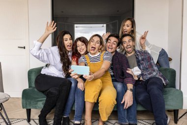 Geniş bir grup orta yaşlı arkadaş evdeki kanepede akıllı telefonlarıyla komik selfie çekiyorlar.