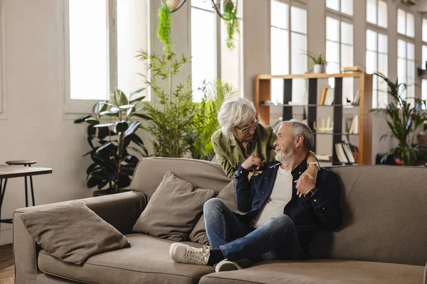 stock image Gray-haired grandparents pose at home. Loving wife hugs husband sitting on the couch, they spend time together. Happy and lasting marriage, harmonious relations between the spouses, respect and bond.