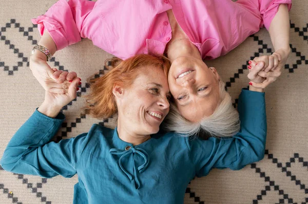 stock image two mature women lying upside down on carpet looking at camera, smiling lesbian women