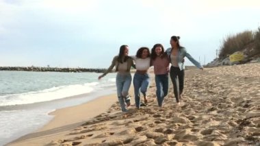 Sahilde mutlu mesut yürüyen, kumsalda eğlenen bir grup kadın.