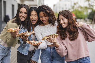 Şehirde pizza yiyen çok ırklı bayan arkadaşlar.