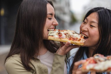 Kadın arkadaşlar dışarıda pizza yiyorlar - çok ırklı kadınlar şehirde sokak yemeklerinin tadını çıkarıyorlar - İtalyan yemek kültürü ve yaz tatili konsepti