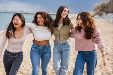 Sahilde mutlu mesut yürüyen, kumsalda eğlenen bir grup kadın.