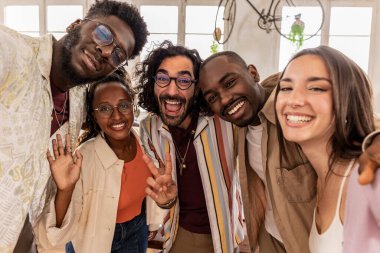 Bir grup neşeli ortak ırk çalışanı arka ışıklandırılmış çatı katında akıllı telefon kullanarak selfie çekiyorlar.