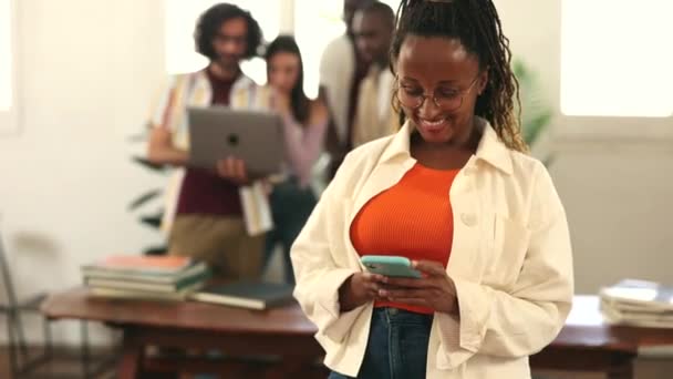 办公室里的非洲妇女用手机进行了自信的交谈 而她的同事则站在后面 被她的说服性话语所吸引 并钦佩她的专业能力 — 图库视频影像