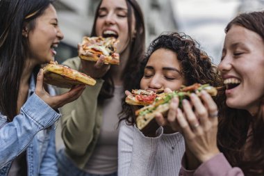 Caddelerde pizza yiyen neşeli çok ırklı kadınlar mutlu milenyum bayan arkadaşları bir İtalyan şehrini ziyaret ederken birlikte hafta sonunun tadını çıkarıyorlar. -